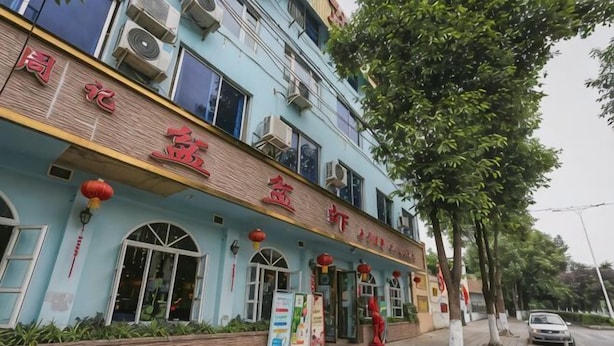 A building with a sign in a foreign language, windows, and a sidewalk with trees. - Xinping Hotel (Dayi)