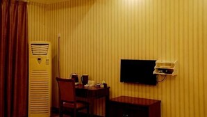 A hotel room with striped wallpaper, a flat-screen TV mounted on the wall, a desk with a chair, and a heater. - Xinping Hotel (Dayi)