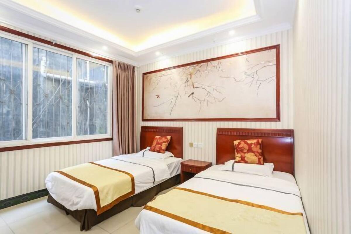 A hotel room with two beds, a large window, and a wall painting.