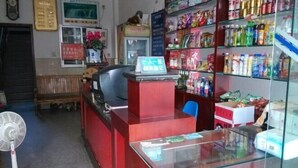 A small shop with a red counter, a fan, and shelves stocked with snacks and drinks. - Xinping Hotel (Dayi)
