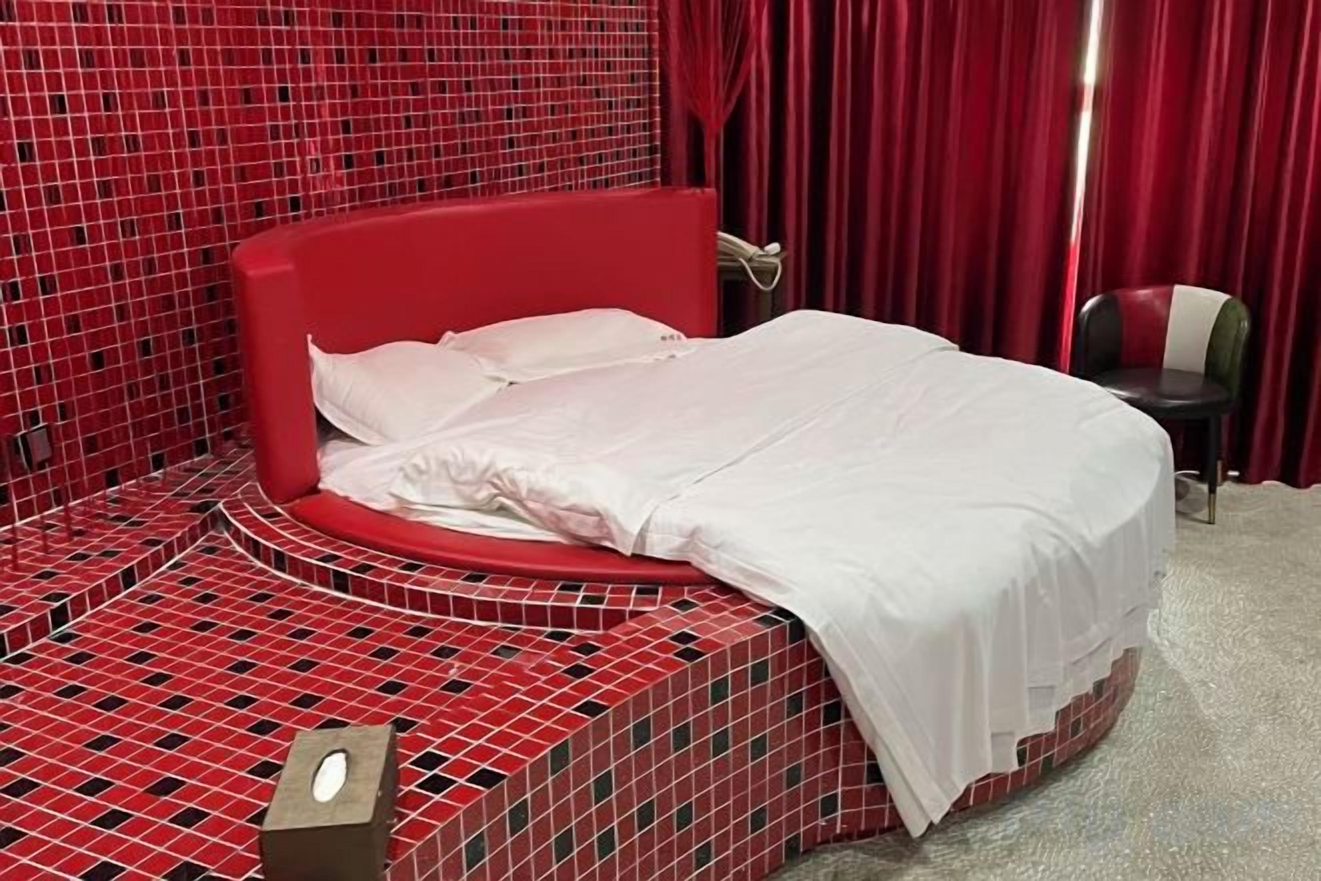 A bed with a red headboard in a room with a red and black checkered floor pattern.