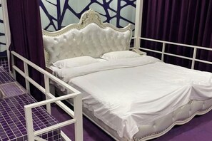Una cama blanca con cabecera decorativa, estructura de metal blanco y un telón de fondo morado.
