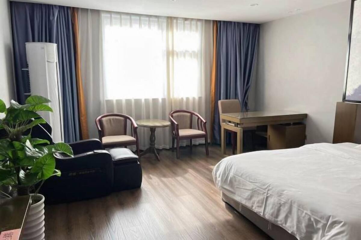 Hotellihuone, jossa on sänky, työpöytä, kaksi tuolia, pieni pöytä, ruukkukasvi ja ilmastointilaite.