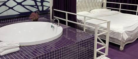 A bathroom with a large bathtub, a white bed, and a decorative wall.