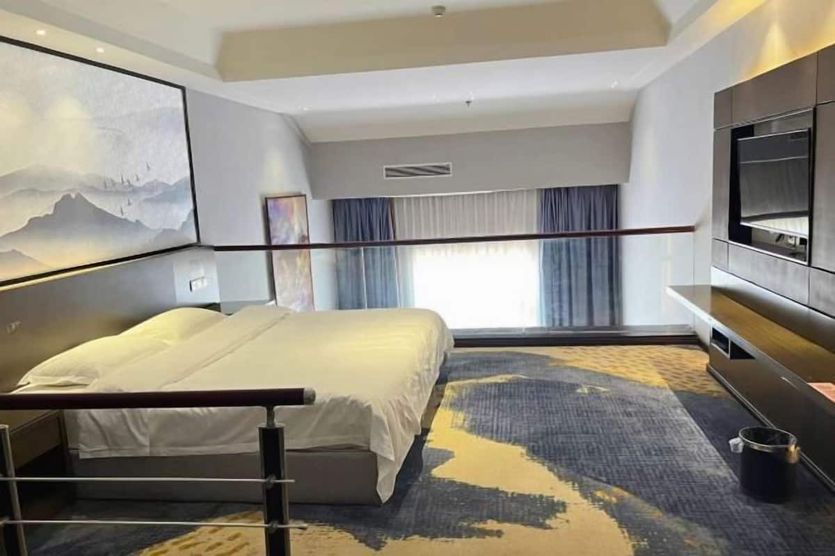 Moderni hotellihuone, jossa on suuri sänky, taulutelevisio ja taulu seinällä.