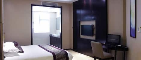 A hotel room with a bed, a desk with a computer, a TV, and a chair.