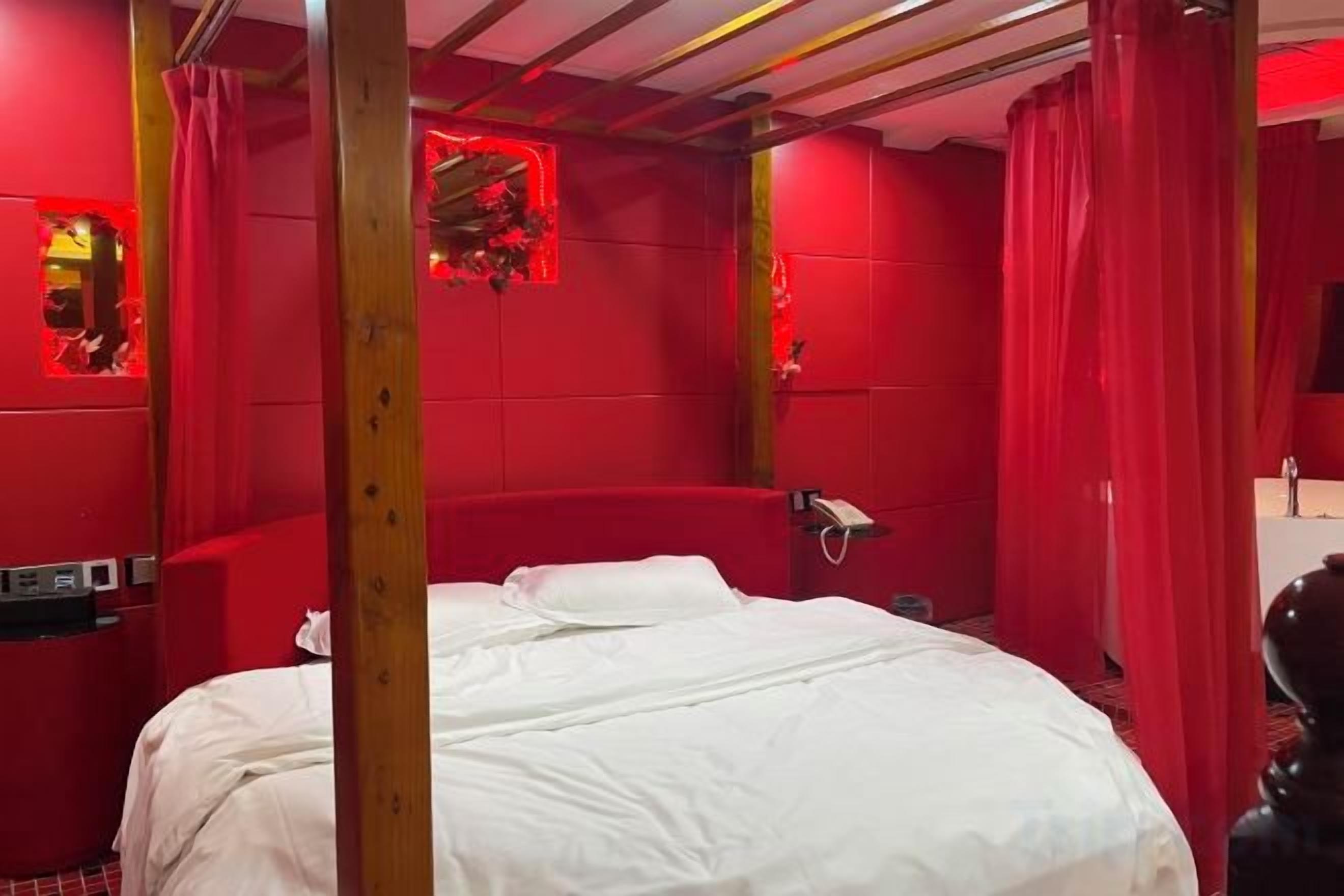 A room with a bed, red walls, and a wooden ceiling structure.