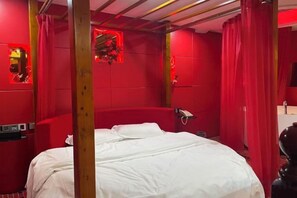 Una habitación con cama, paredes rojas y estructura de techo de madera.