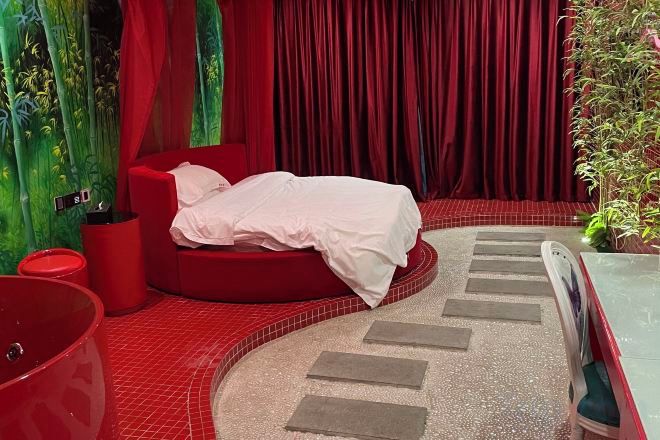 A red-themed bedroom with a bed, a red chair, and a small table.
