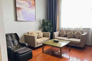 A living room with two beige sofas, a black massage chair, a glass coffee table, and a large abstract painting on the wall. - Poyang Yishang · Wanjing Business Hotel (Poyang)