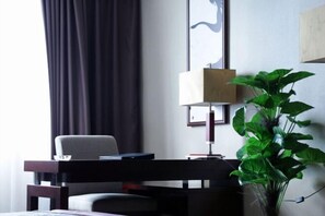 Una habitación con cortina oscura, una silla, un escritorio con lámpara y una planta en maceta.