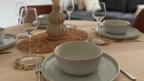Una mesa de comedor dispuesta con platos, fuentes, cubiertos y un florero con plumas.