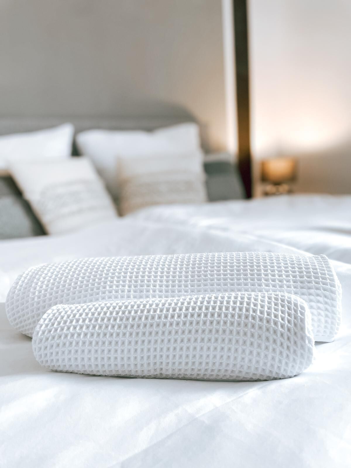 Un lit bien fait, avec du linge de lit et des oreillers blancs, une table de chevet avec une lampe et une fenêtre avec des rideaux.