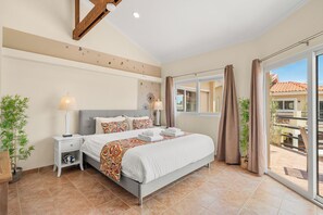 Une chambre à coucher avec un lit, des tables de chevet, une lampe, une fenêtre avec des rideaux et une vue sur l’extérieur.