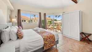 Ein Schlafzimmer mit Bett, Nachttisch, Lampe, Fenster, Balkon mit Blick auf Häuser und Kleiderschrank.