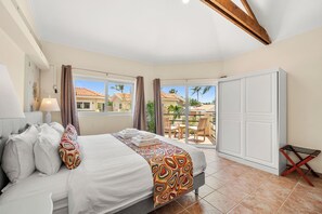 Une chambre avec un lit, une table de chevet, une lampe, une fenêtre, un balcon donnant sur des maisons et une armoire.