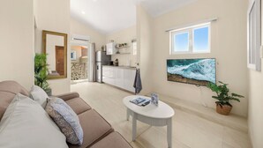 Ein Wohnzimmer mit Sofa, Couchtisch, Fernseher und einer Küche im Hintergrund.