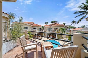 Een balkon met een zwembad, stoelen en uitzicht op omliggende huizen.
