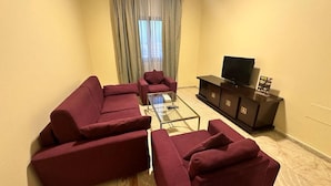 Una sala de estar con un sofá modular, una mesa de centro de vidrio, un televisor de pantalla plana y un mueble de madera oscura.