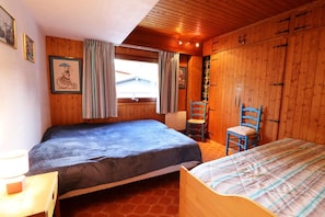 Una habitación acogedora con paredes de madera, dos camas, una silla y un ventanal con cortinas.