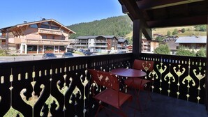 Un balcone con vista su una montagna e degli edifici. Si vedono due sedie rosse e un tavolino.