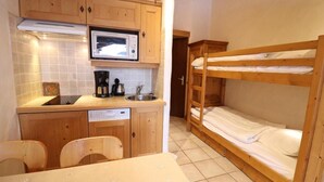 Una cucina compatta con mobili in legno, un forno a microonde, una macchina da caffè e un lavello. C'è un letto a castello con biancheria bianca e un tavolino con tovaglia fantasia.