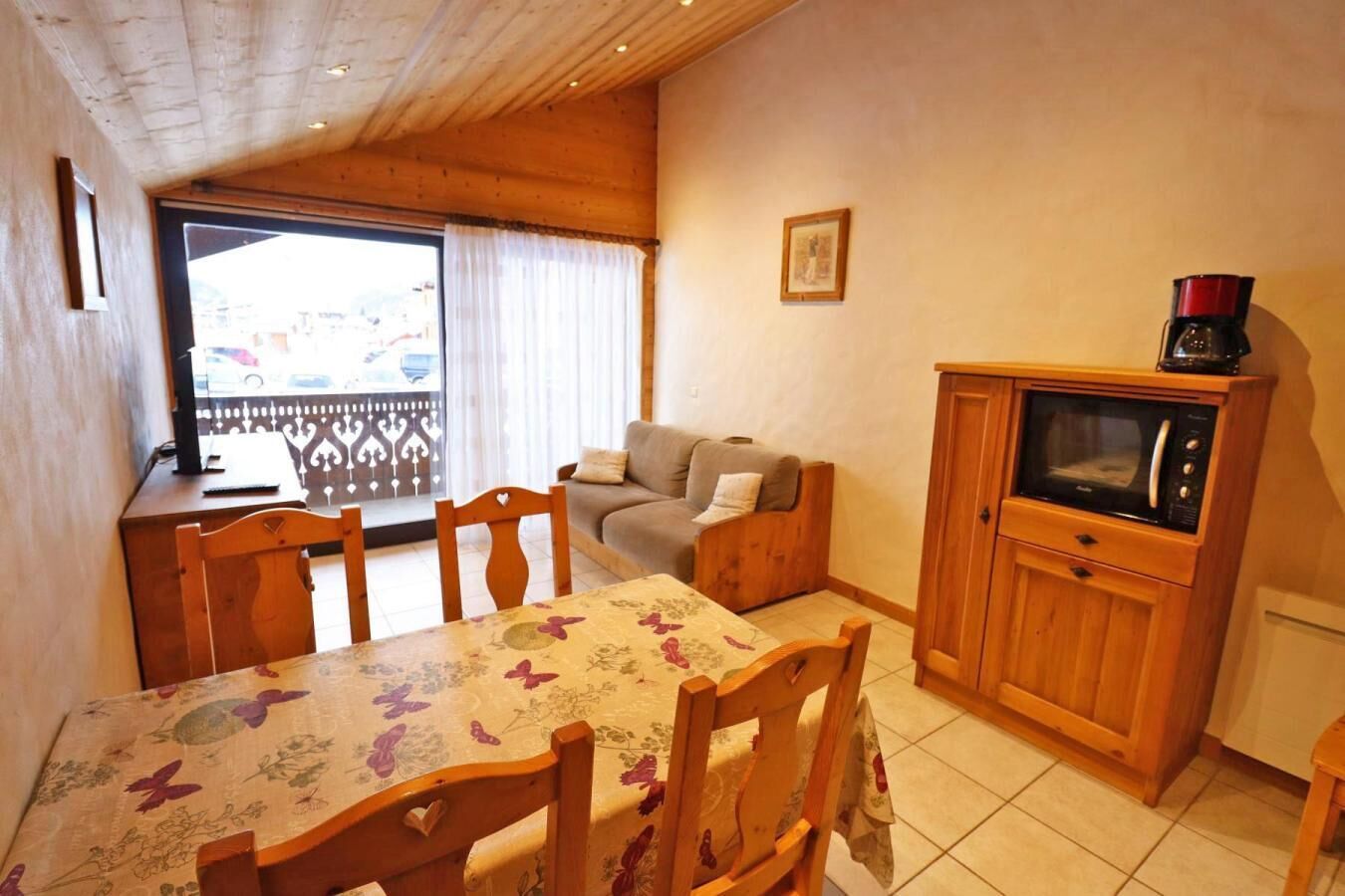 Ein gemütliches Zimmer mit Esstisch, Stühlen, einer Couch, einem Holzschrank mit einer Mikrowelle und einem Fenster mit Blick nach draußen.