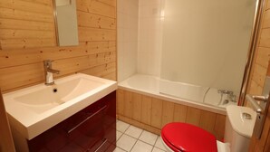 Et badeværelse med træpaneler, en hvid vask, et rødt toilet og en brusekabine med glas.