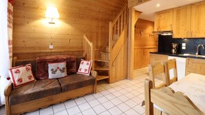 Hyggelig interiør i en hytte med en trætrappe, en sofa med pyntede puder, et spisebord og et køkkenområde.