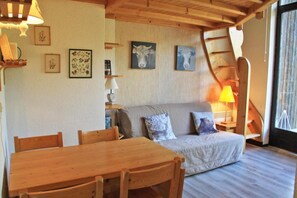 Una habitación acogedora con una mesa y sillas de madera, un sofá con cojines estampados y una escalera que sube a un nivel superior.