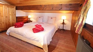 Camera da letto con rivestimento in legno, un letto, due lampade da comodino e una finestra con tenda.