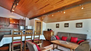 Un accogliente soggiorno con soffitto in legno, un divano grigio con cuscini rossi, un tavolino in legno e un'area pranzo con sedie e tavolo in legno.