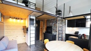 Un espace de vie moderne et compact comprenant une chambre en mezzanine, un coin repas et une cuisine.