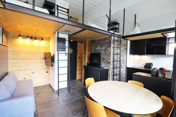 A modern, compact living space with a loft bedroom, a dining area, and a kitchen.