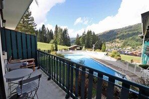 A balcony with a view of a swimming pool, a wooden table, and a chair.