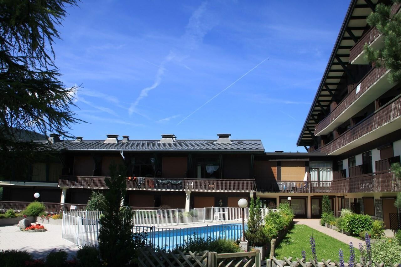 Een hotel met meerdere verdiepingen, balkons, een zwembad en een verzorgde tuin.