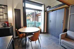 Um espaço compacto com uma mesa de jantar redonda, quatro cadeiras, um sofá, uma cozinha compacta e uma porta deslizante para uma varanda.