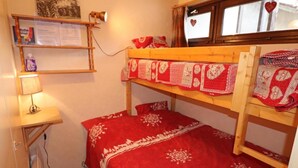 Una cama litera con una manta roja, un escritorio con una lámpara y una estantería con objetos.