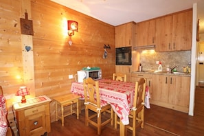 A cozy wooden cabin with a dining table set for four, a microwave, and a stove in the kitchen area. - 300m from resort center, 1st floor, balcony, ski locker, 30m², Les Gets (Les Gets)