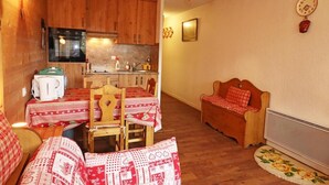 Una sala de estar acogedora con comedor, muebles de madera, un sofá, una mesita y una cocina con armarios y estufa.