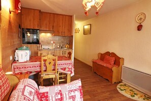 A cozy living room with a dining area, wooden furniture, a sofa, a small table, and a kitchen area with cabinets and a stove. - 300m from resort center, 1st floor, balcony, ski locker, 30m², Les Gets (Les Gets)