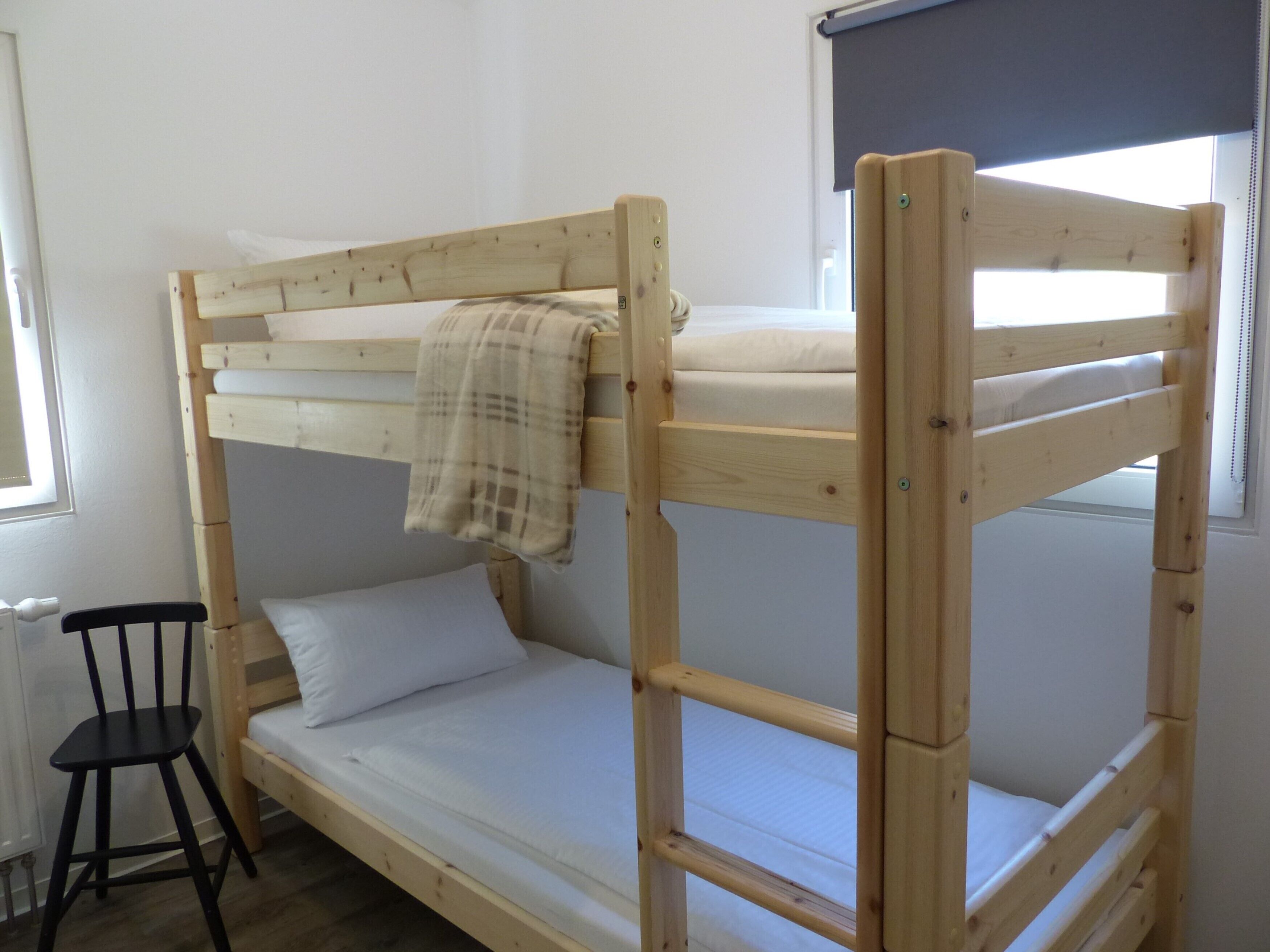 A bunk bed with a wooden frame, a black chair, and a window with blinds.