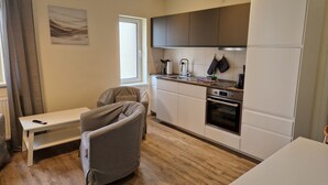 A modern kitchen with a built-in oven, a dining area with a bench, and a window with curtains. - Bernsteinland Barth (Barth)