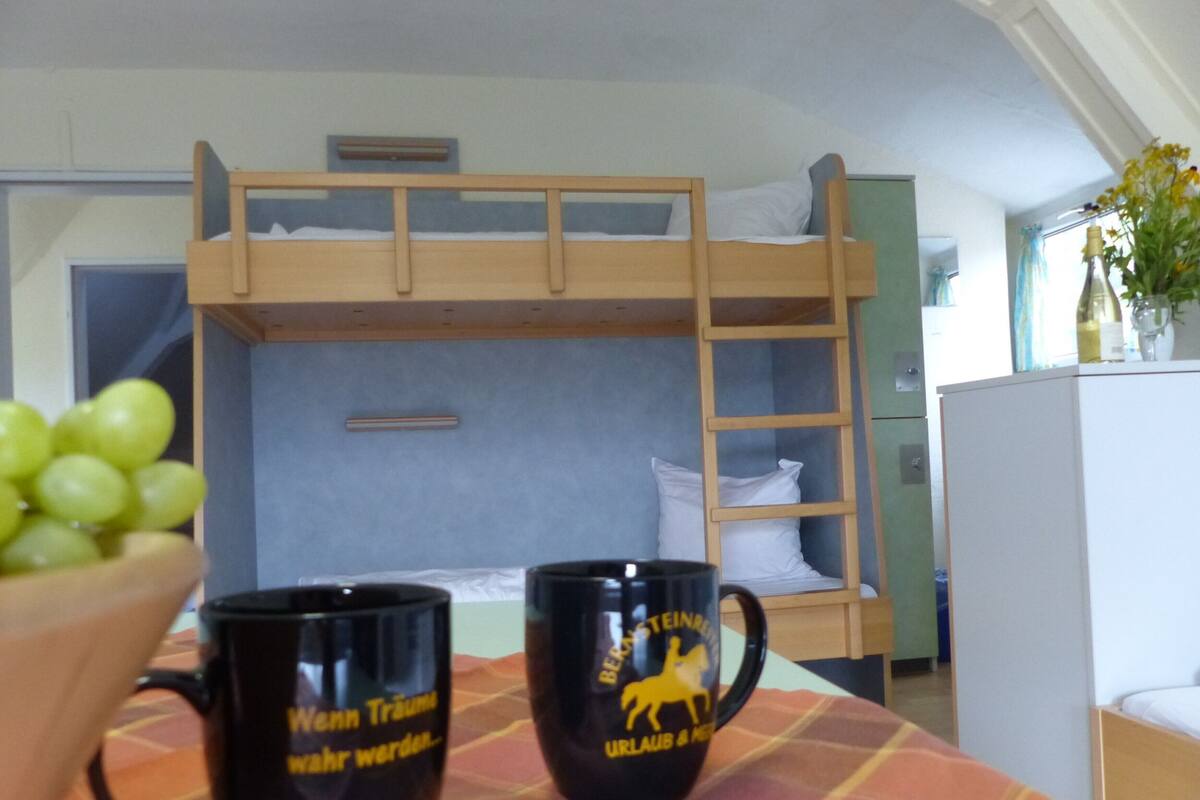 A bunk bed room with a table, two mugs, and a bowl of grapes.