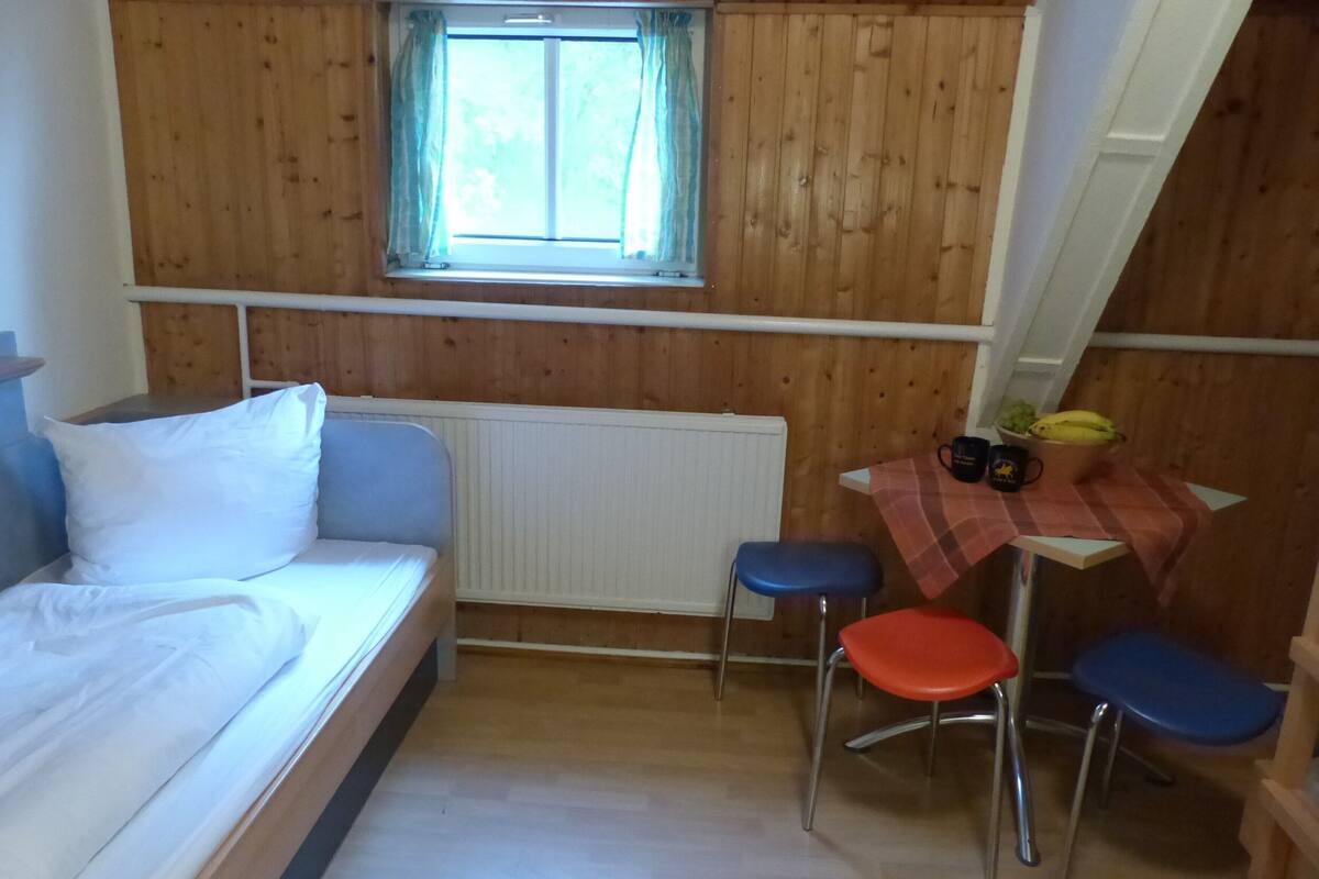 A wooden cabin room with a bed, a table with chairs, and a window with curtains.