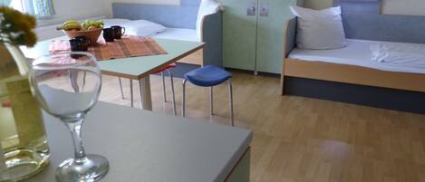 A room with a bed, a table with a bowl of fruit, a glass of water, and a cabinet.