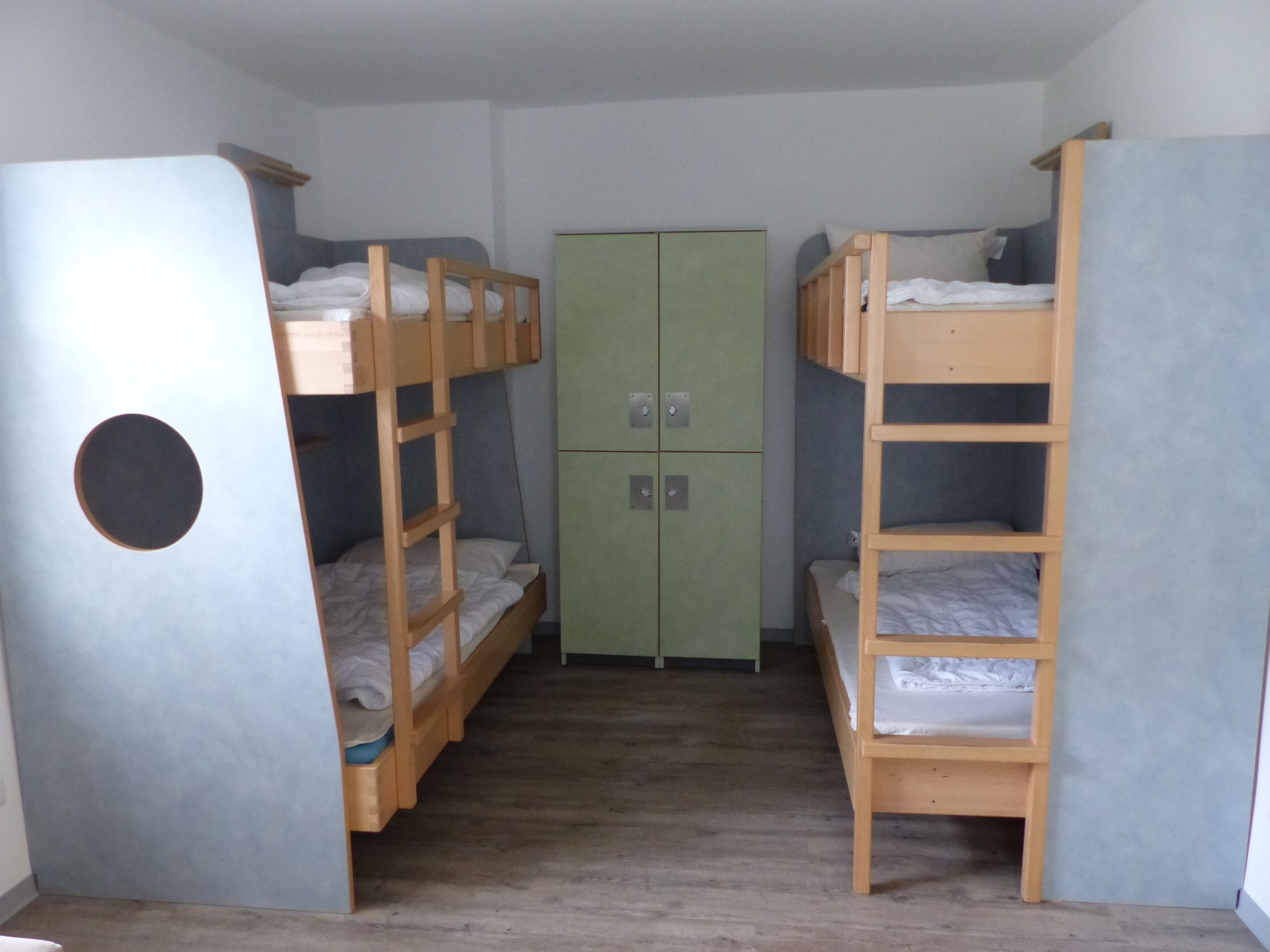 Een slaapzaal met stapelbedden, een groene kast en een klein tafeltje.