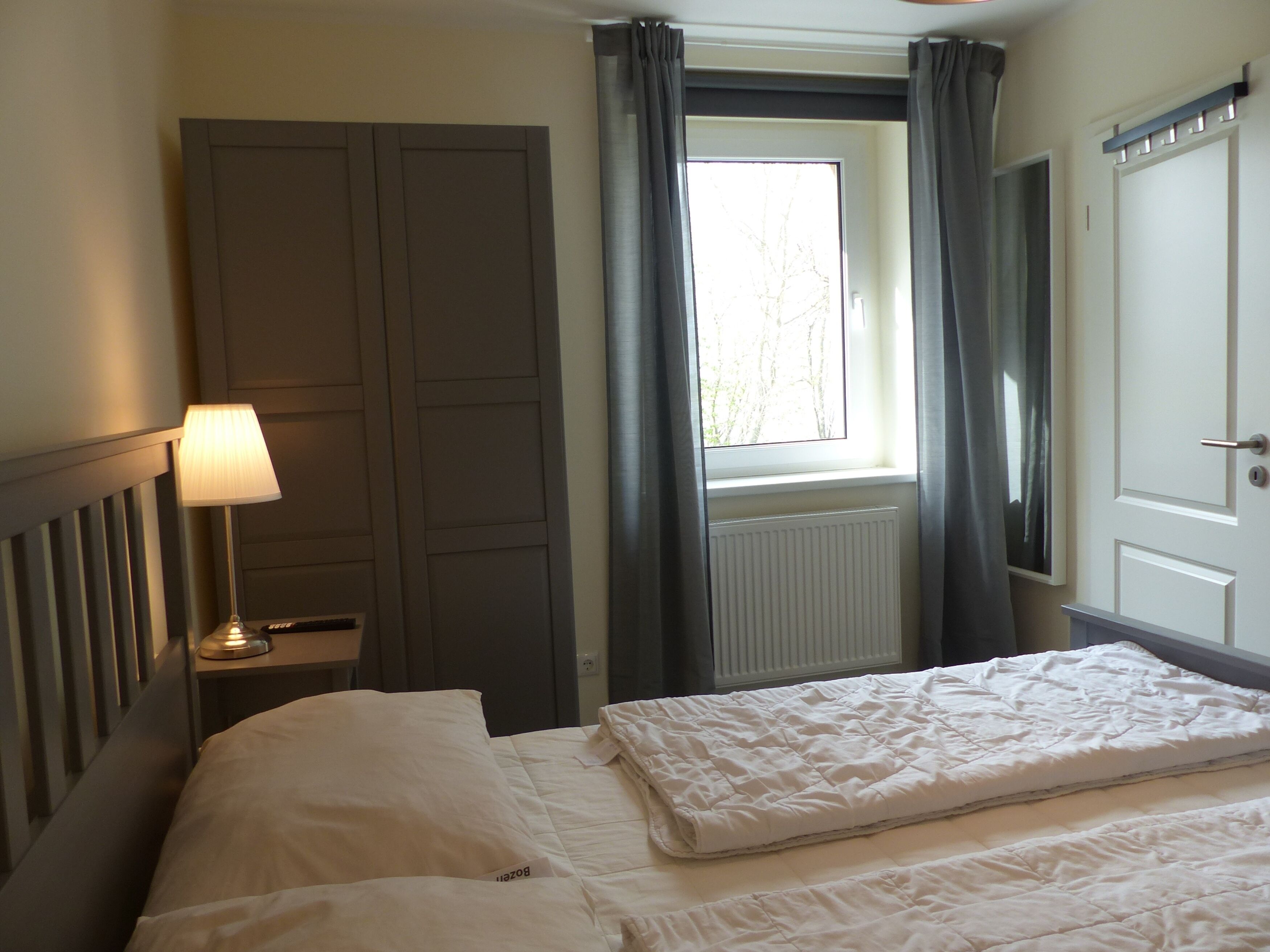 Una camera d'albergo con un letto, un comodino con una lampada, una finestra con tende e una porta.