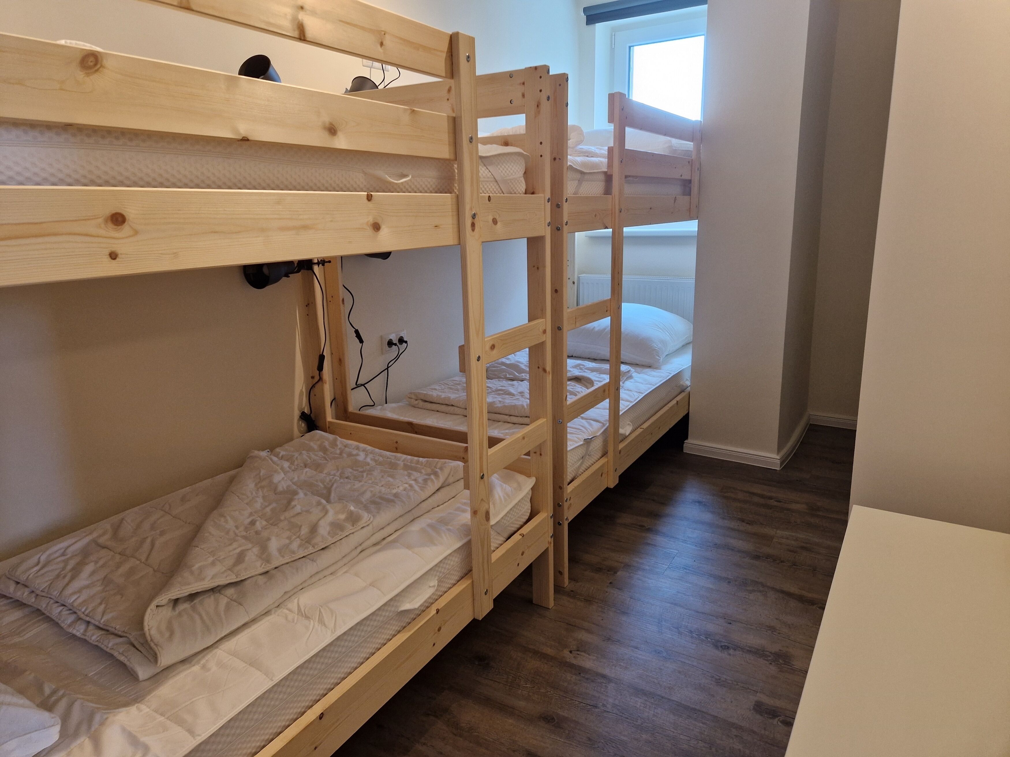 A room with three bunk beds, wooden flooring, and a window with blinds.