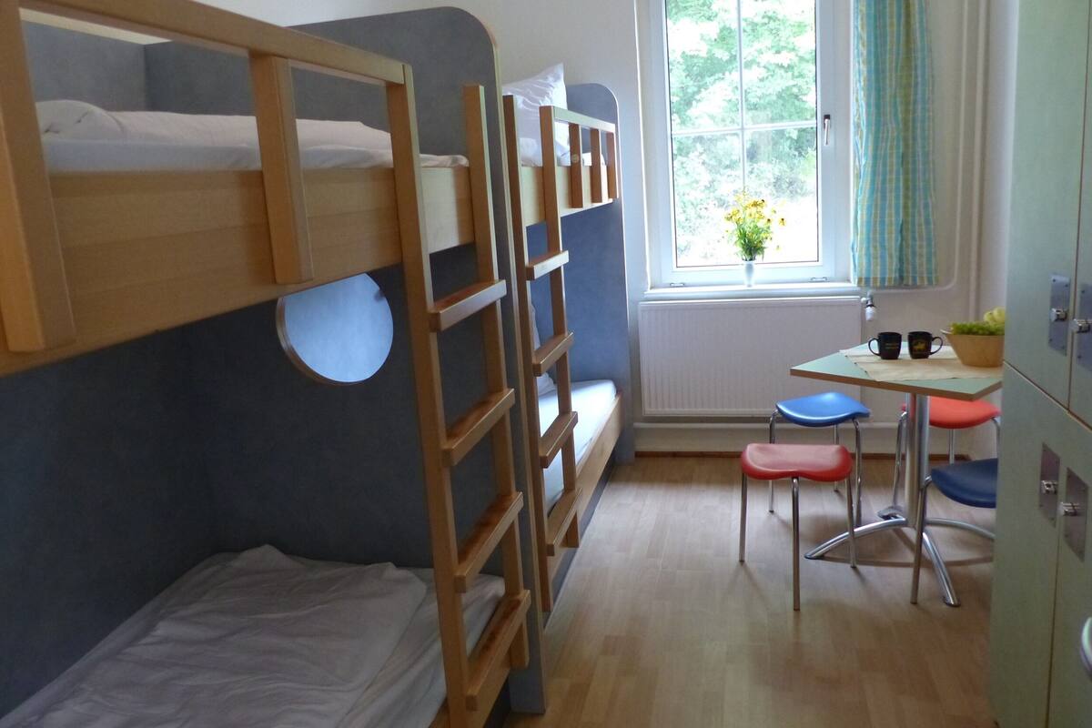 A bunk bed room with a small desk and two chairs.